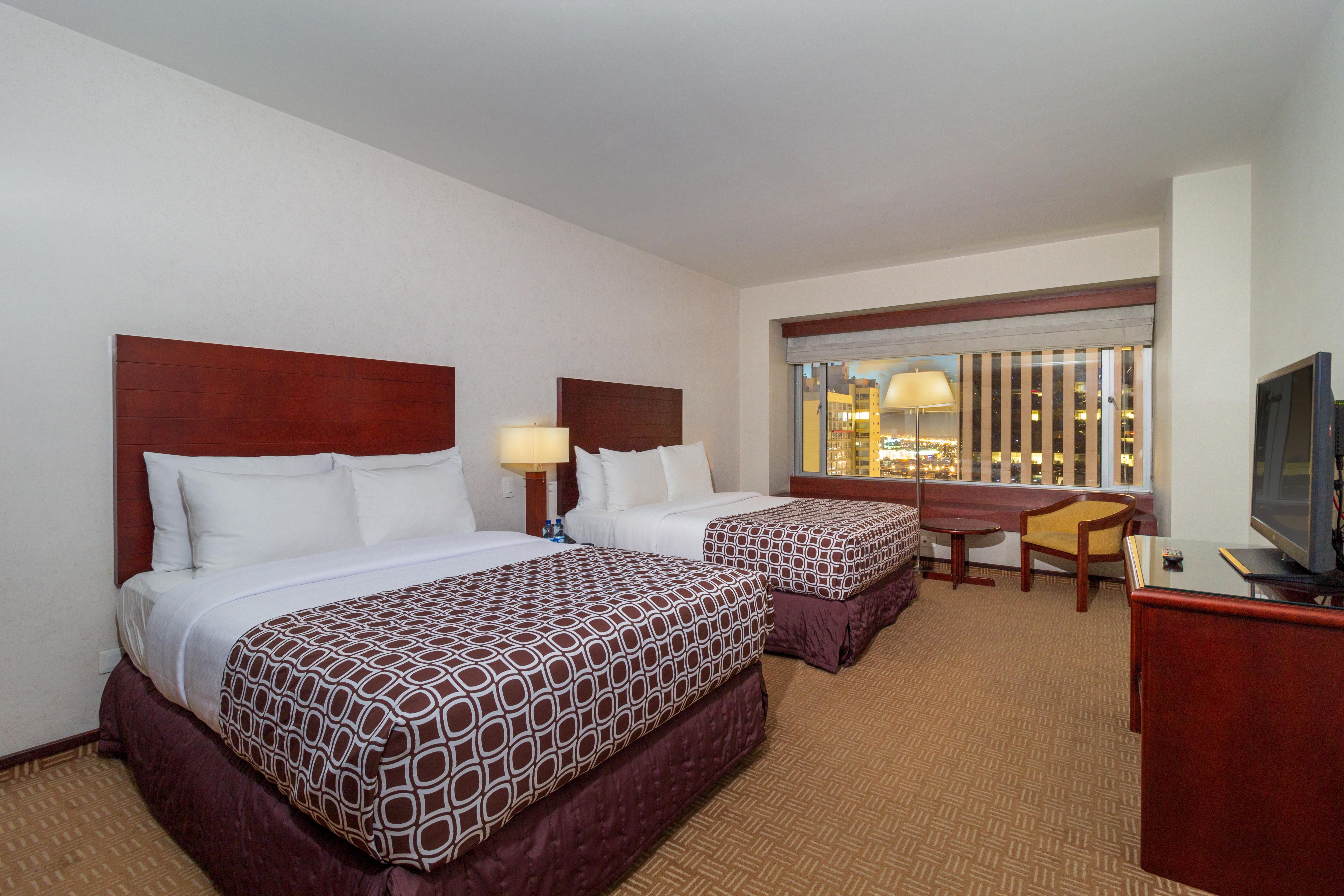 GHL Hotel Tequendama Bogotá Exterior foto The photo shows a hotel room featuring two beds with white linens and patterned bedspreads in dark tones. There is a bedside lamp next to one of the beds. A window is visible, providing light to the room, and it appears to offer a view outside. Addit