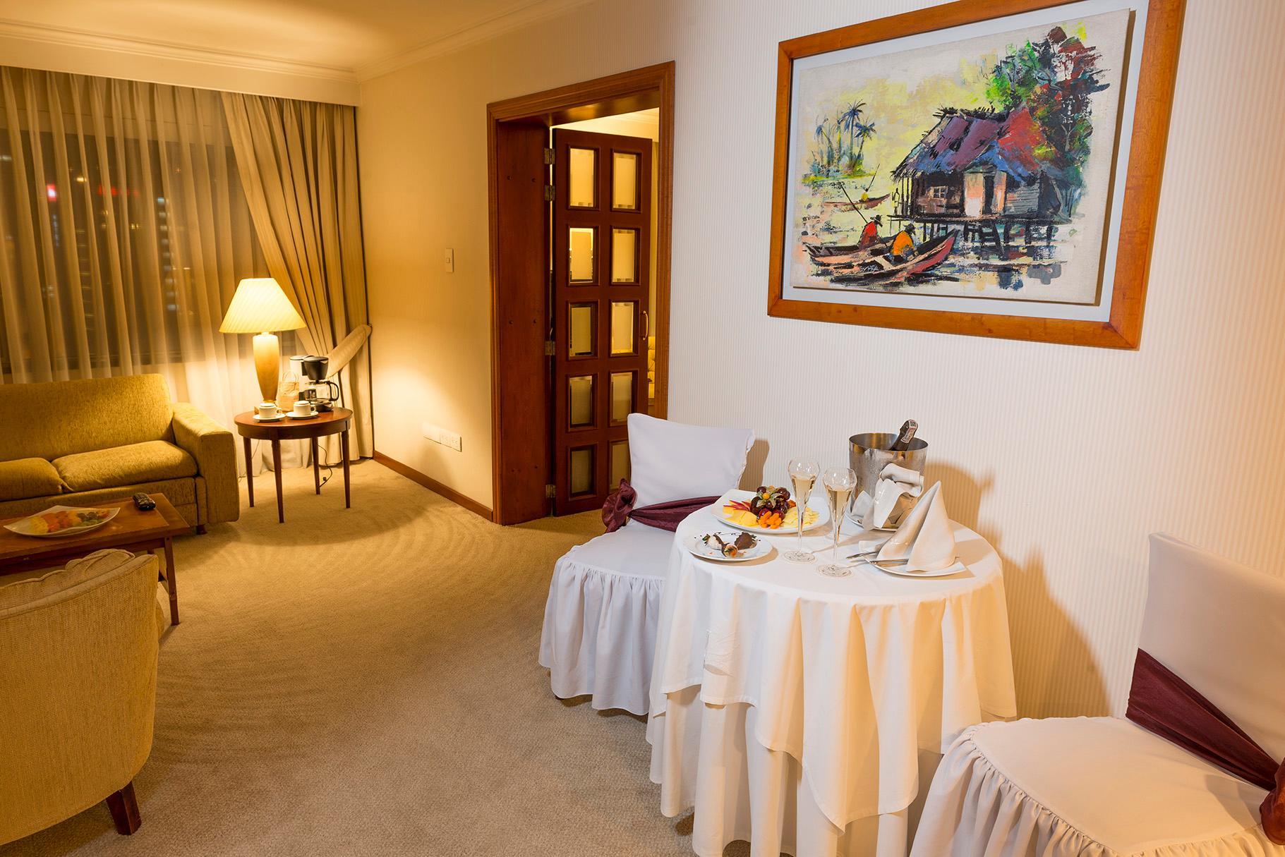 GHL Hotel Tequendama Bogotá Exterior foto The photo shows a cozy hotel room or suite. It features a seating area with a comfortable armchair and a small round table. There is a decorative table with a white tablecloth, on which a tray with drinks and fruit is placed. The walls are adorned wi
